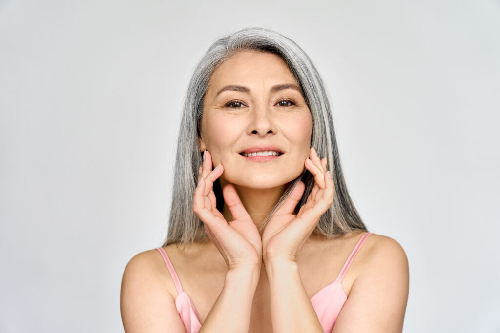 Confident mature woman with long gray hair smiling and touching her face